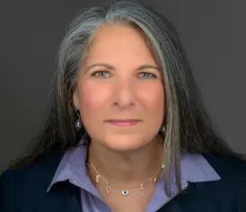 A woman with long grey hair wearing a blue shirt.