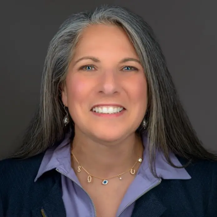 A woman with long gray hair and wearing a blue shirt.